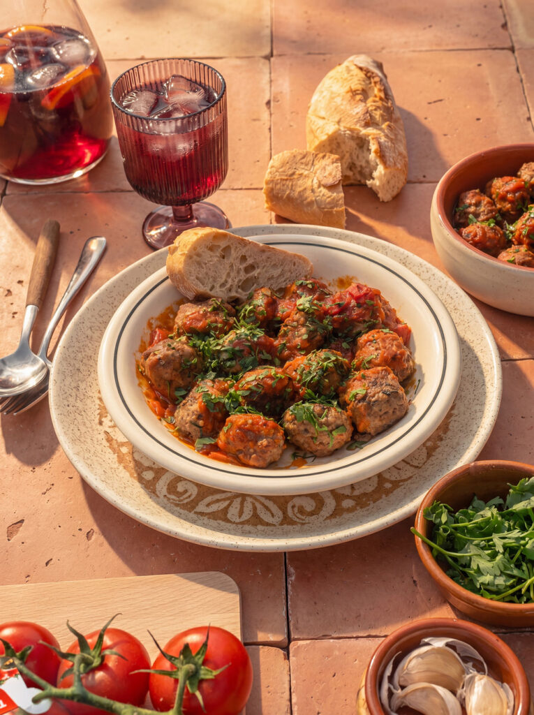 Een schaal Spaanse albóndigas in Tasty Tom tomatensaus op een gedekte tafel.