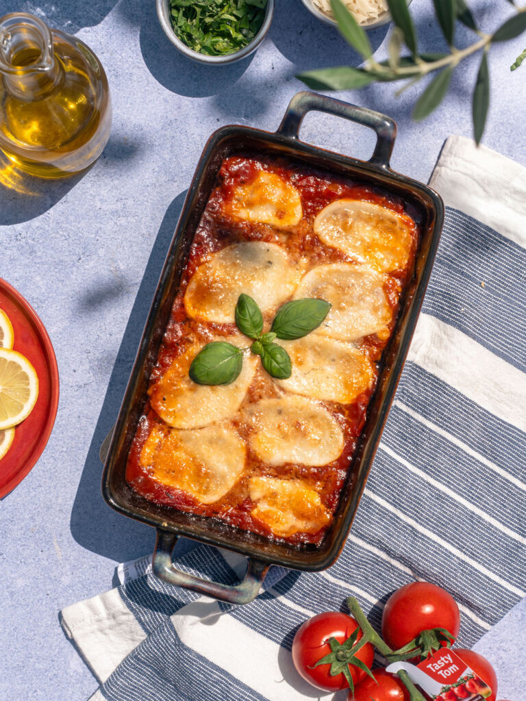 Een ovenschaal met Melanzane met Tasty Tom saus op een zonnige gedekte tafel